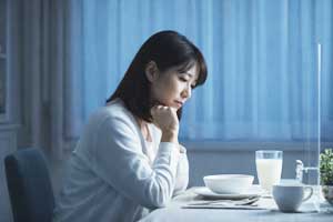 夕食中に夫と向き合いながらも、自分の考えに耽ってしまい、心の距離を感じている40代の日本人女性。夫婦の会話で本音が言えず自分をチェックしている様子